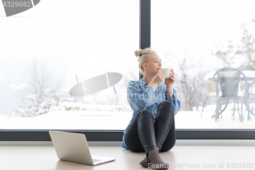 Image of woman drinking coffee and using laptop at home