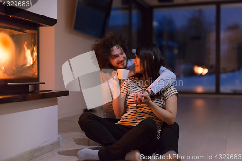 Image of happy multiethnic couple sitting in front of fireplace