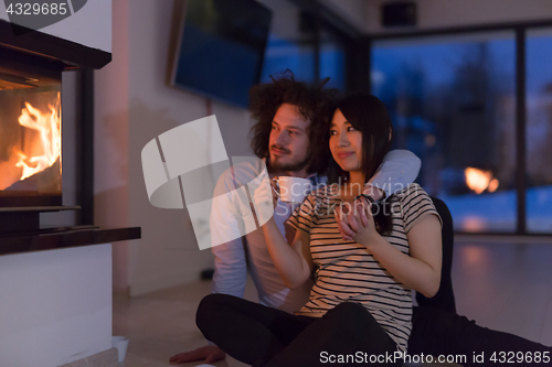Image of happy multiethnic couple sitting in front of fireplace