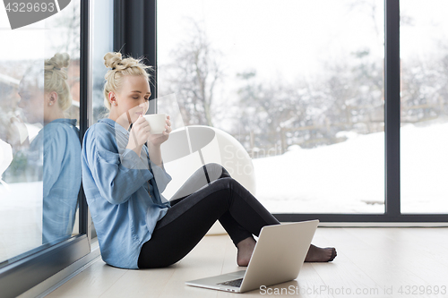 Image of woman drinking coffee and using laptop at home