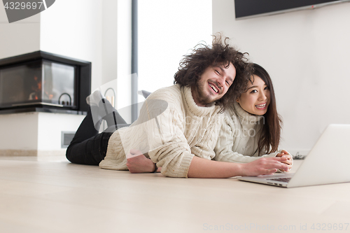 Image of young multiethnic couple using a laptop on the floor