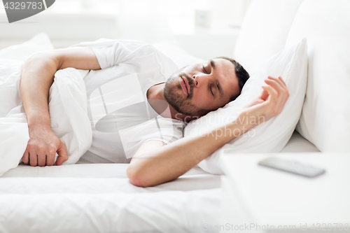 Image of man sleeping in bed with smartphone on nightstand