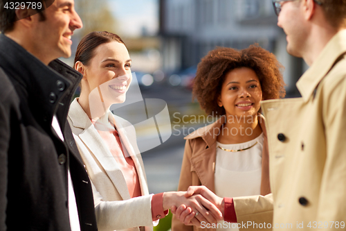 Image of happy people shaking hands on city street