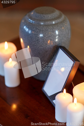 Image of photo frame, cremation urn and candles on table