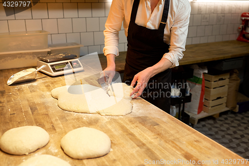 Image of baker portioning dough with bench cutter at bakery