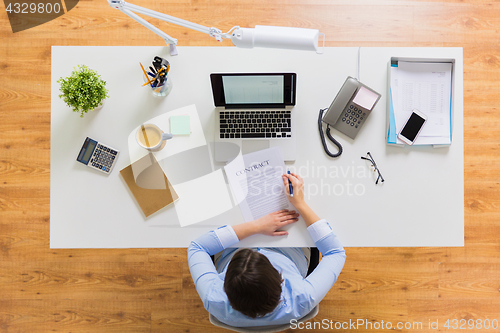 Image of businesswoman signing contract document at office