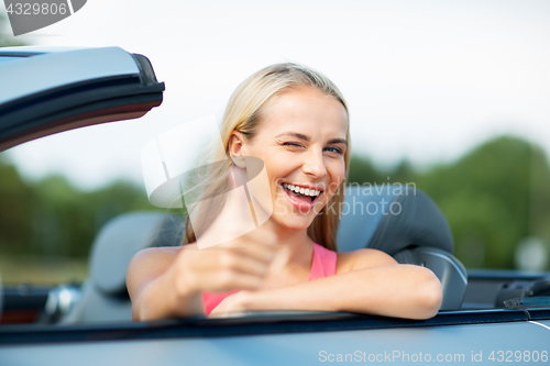 Image of happy young woman in convertible car thumbs up