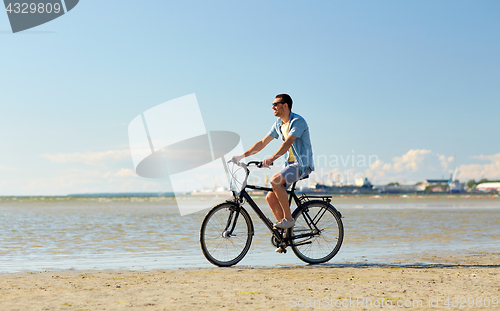 Image of happy man riding bicycle along summer beach