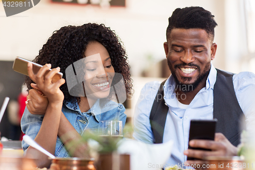 Image of happy man and woman with smartphones at restaurant