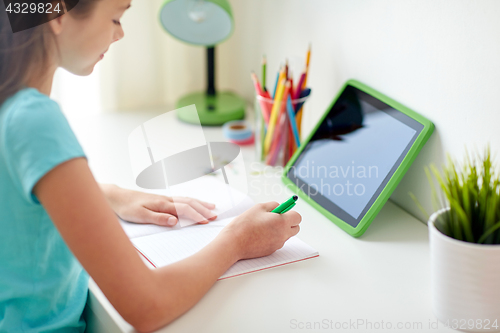Image of girl with tablet pc writing to notebook at home