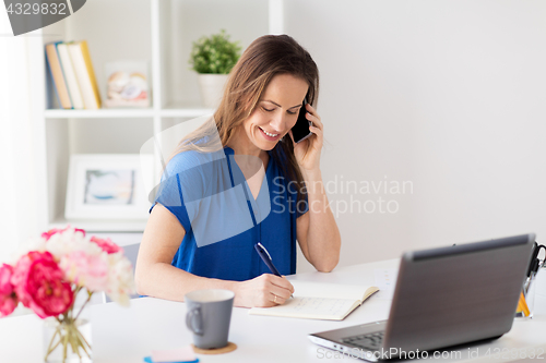 Image of woman with notepad calling on smartphone at office
