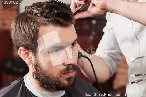 Image of The hands of barber making haircut to young man in barbershop