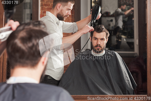 Image of Young handsome barber making haircut of attractive man in barbershop