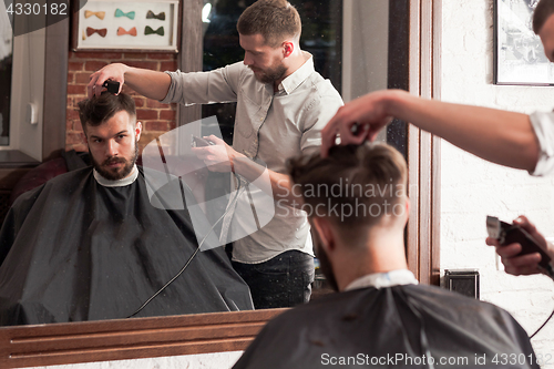 Image of Young handsome barber making haircut of attractive man in barbershop