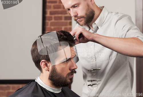 Image of Young handsome barber making haircut of attractive man in barber