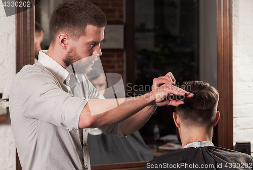 Image of Young handsome barber making haircut of attractive man in barbershop