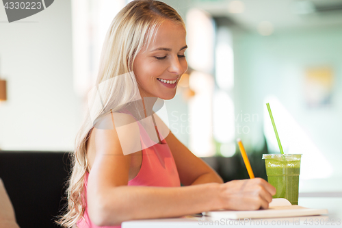 Image of woman with drink writing to notebook at restaurant