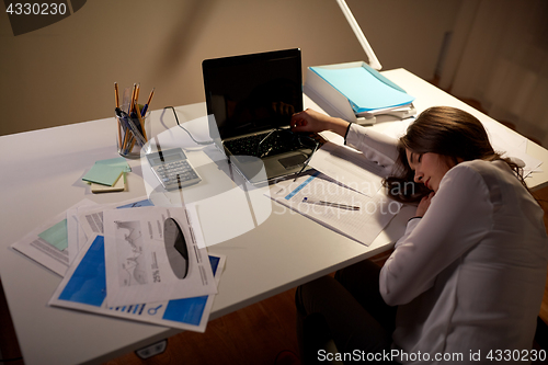 Image of tired woman sleeping on office table at night