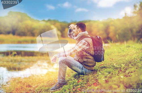 Image of smiling man with backpack resting on river bank