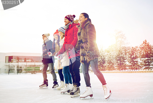 Image of happy friends ice skating on rink outdoors