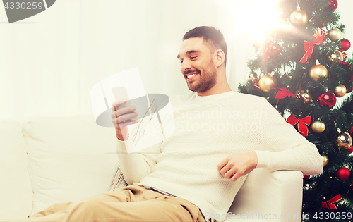 Image of smiling man with smartphone at home for christmas