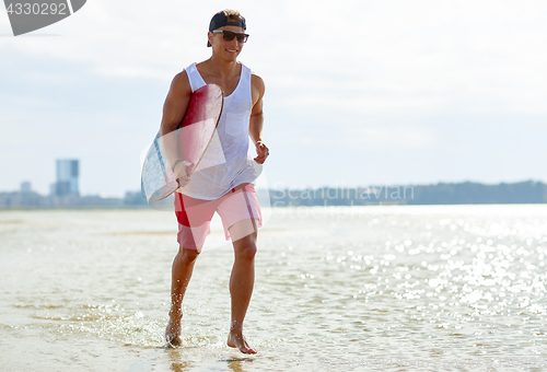 Image of happy young man with skimboard on summer beach