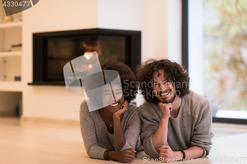 Image of multiethnic couple lying on the floor  in front of fireplace