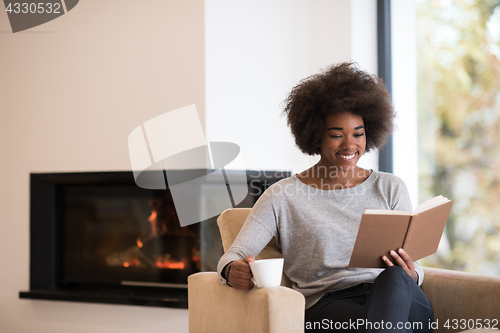 Image of black woman reading book  in front of fireplace