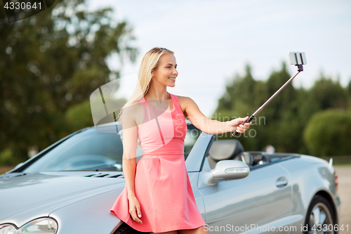 Image of woman taking picture by selfie stick at car