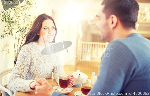 Image of happy couple with tea holding hands at restaurant