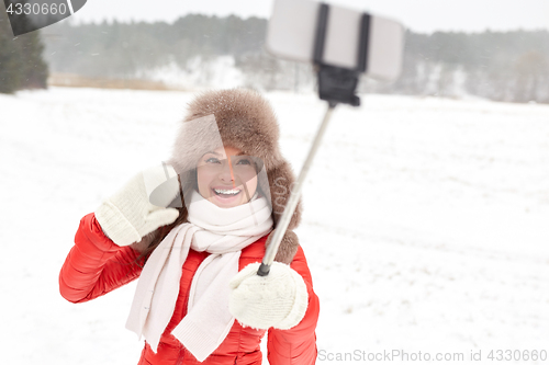 Image of happy woman with selfie stick outdoors in winter