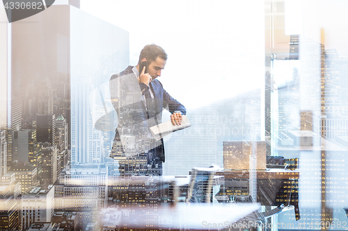 Image of Businessman talking on mobile phone while looking at wristwatch.