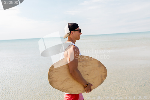 Image of happy young man with skimboard on summer beach