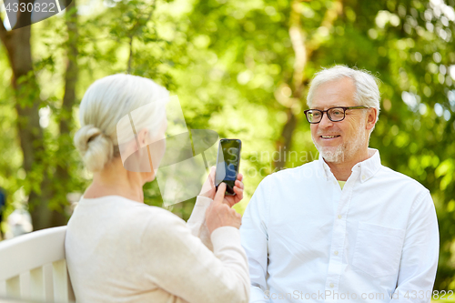 Image of old woman photographing man by smartphone in park