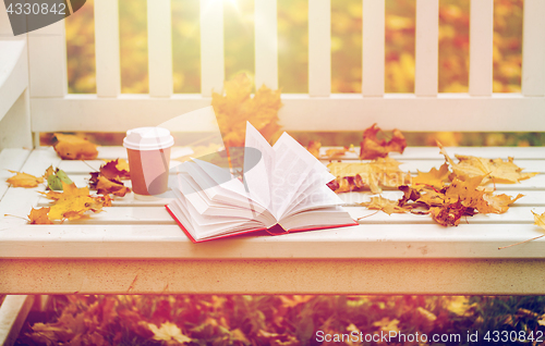 Image of open book and coffee cup on bench in autumn park