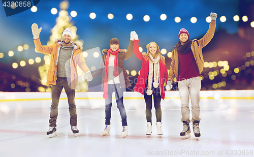 Image of happy friends waving hands on outdoor skating rink