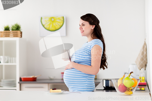 Image of happy pregnant woman with mug and cake at home