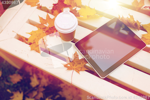 Image of tablet pc and coffee cup on bench in autumn park
