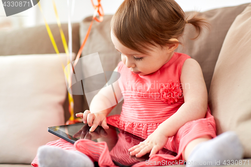 Image of baby girl with tablet pc sitting on sofa at home