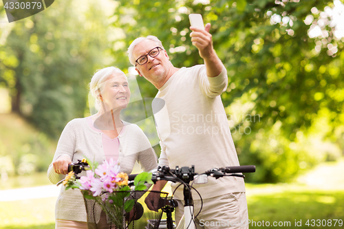 Image of senior couple with bicycles taking selfie at park