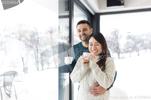 Image of multiethnic couple enjoying morning coffee by the window