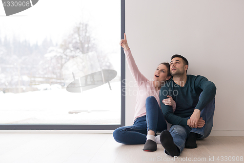 Image of young couple sitting on the floor near window at home