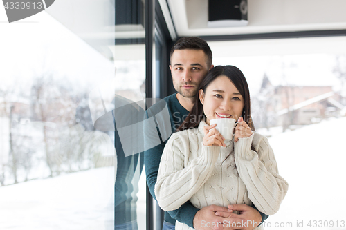 Image of multiethnic couple enjoying morning coffee by the window