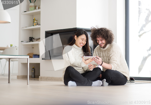 Image of multiethnic couple using tablet computer in front of fireplace