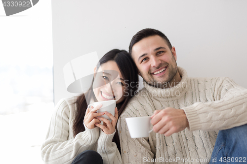Image of multiethnic couple enjoying morning coffee by the window