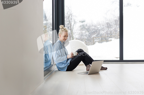 Image of woman drinking coffee and using laptop at home