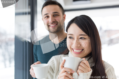 Image of multiethnic couple enjoying morning coffee by the window