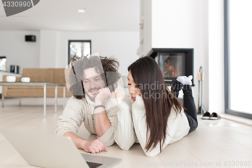 Image of young multiethnic couple using a laptop on the floor