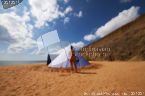 Image of Blurred view of conical tent and sunbathing girl on summer beach