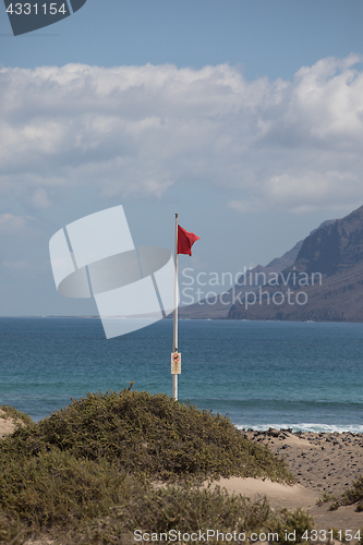 Image of The red flag weighs in the wind at Surfers Beach Famara on Lanza